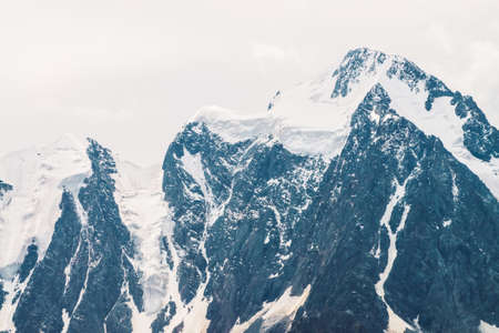 Amazing huge glacier top snowy mountain range in overcast sky wonderful giant rocky ridge with snow in mist atmospheric minimalist landscape of majestic nature of highlands tranquil mountainscape Фото со стока