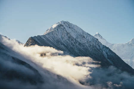 Beautiful view of snow capped mountains above thick clouds in sunshine scenic bright mountain landscape with white snow peak among dense low clouds in blue sky wonderful scenery with snowy pinnacle