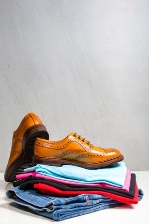 Pair of male full brogued tan oxford shoes placed on top of heap of clothing vertical image composirion Stock Photo