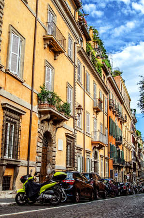 Strada romana con belle case colorate. Molte macchine sono parcheggiate sotto le case lungo la strada.