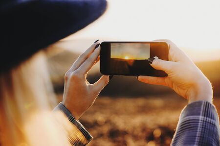 Young blonde female traveler taking a picture of an epic sunset while traveling in her spring vacation time Stock Photo