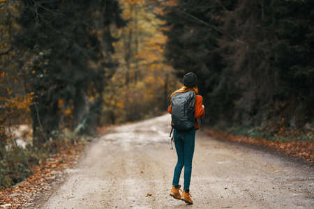 Happy traveler with backpack walks on the road in autumn forest