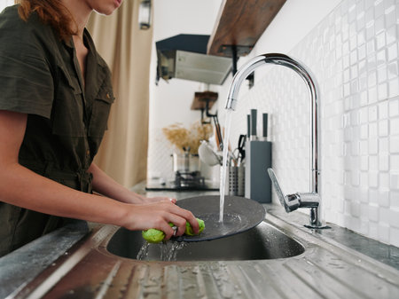 Woman with hands without gloves washes dishes with a dishwashing sponge household chores no dishwasher high water consumption close up of hands