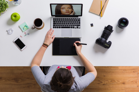 Woman with camera working on laptop at table Stock Photo