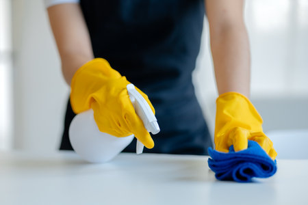 Limpieza de la superficie del escritorio en la oficina con desinfectante en aerosol, use guantes y limpie la mesa con una toalla, el ama de llaves está limpiando el escritorio por higiene debido a la idea de limpieza de covid 19 Foto de archivo