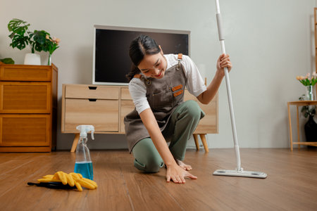 Housewife is mopping the floor in the house to remove dust and keep it hygiene for everyone in the family safe a wife is wearing apron to clean and make the living room neat Foto de archivo