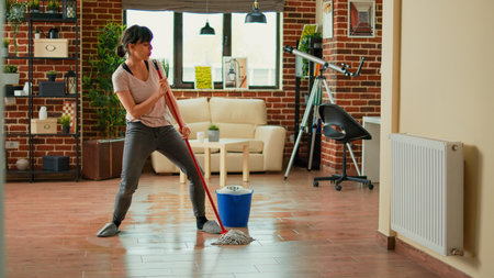 Happy funny person mopping floors with all purpose cleaner and dancing spring cleaning young cheerful housewife using mop to sweep dirt and clean mess listening to music at home Foto de archivo