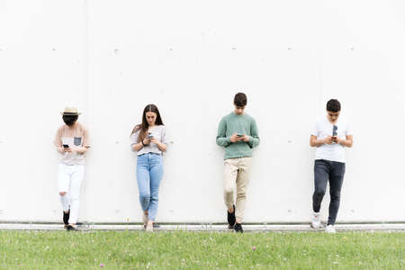 Teenagers against a wall using their phones students concentrated on social media digital addiction and social distancing concept Stock Photo