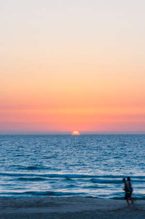 Vista al mar al atardecer con siluetas de deportistas corriendo Foto de archivo