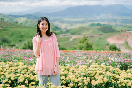 분홍색 셔츠를 입은 아시아의 아름다운 여성이 뒤에 있는 노란 꽃밭에 행복하게 웃고 서 있는 것이 산의 경치입니다 스톡 콘텐츠