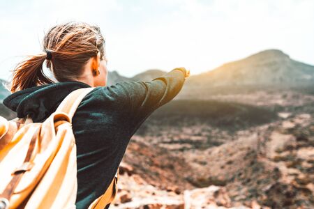 Young woman hiking on the top of the mountain pointing with the finger at the sunset