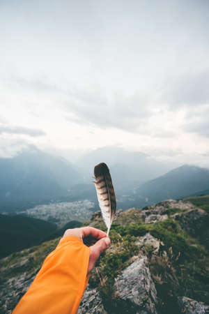 Hand holding bird feather moody mountains landscape aerial view travel adventure lifestyle concept freedom and solitude emotions harmony with nature