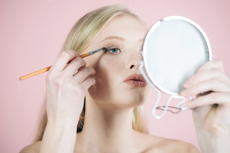 Girl model with makeup brush near face skin care products woman with blue eyes applying makeup using makeup brush and look in mirror light make up natural beauty skincare facial treatment concept