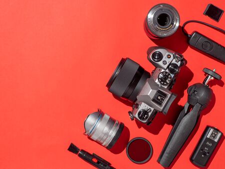 Photographer workplace with dslr camera lens pen tablet and camera accessories on red background camera photography visual content concept flat lay or top view copy space hard light