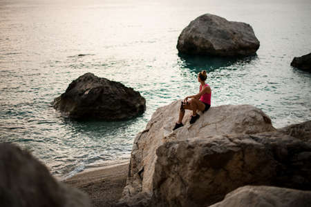 View of woman sitting on huge stone on the seashore and looking away