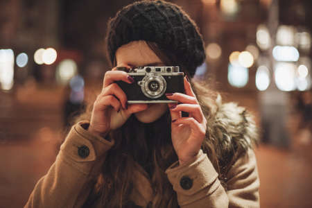 Hipster girl with retro camera taking photos in the night city street Stock Photo