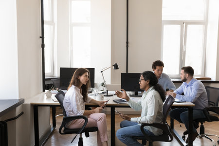 Pairs of busy multiethnic office colleagues talking at shared workplace table collaborating on startup project sharing ideas hr recruit managers interviewing job candidates in coworking