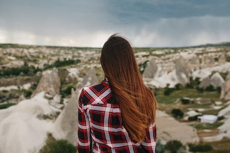 Een jonge vrouw staat op een hoog punt en kijkt naar het uitzicht op de heuvels van Cappadocië bij regenachtig weer.