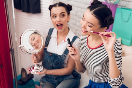 Two fashion blogger girls in jeans and shirt with skirt hold up mascara and mirror to camera