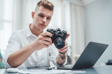 Businessman dressed in formal clothing uses his photocamera sitting at the table there are his laptop and other things career and success