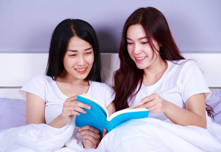 Two woman reading a book on bed in the bedroom Stock Photo