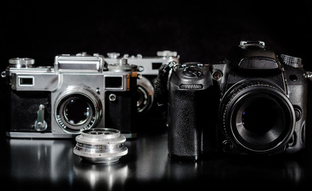 Two vintage cameras with lens and one modern camera on a black background closeup