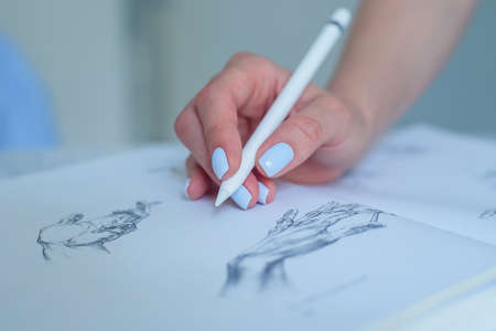 Woman holding digital pen and pointing at pencil sketches in the book