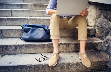 Detail of modern hipster man´s feet sitting on the stairs and using laptop