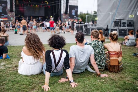 Vista trasera del grupo de jóvenes amigos en el festival de verano, sentados en el suelo. Foto de archivo