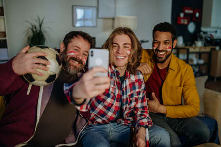 Felices amigos aficionados al fútbol viendo fútbol en casa y tomando selfie