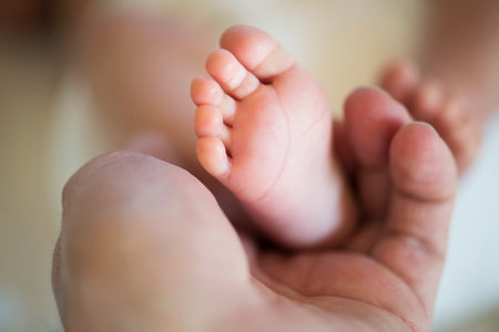 Parent holding small feet of little baby lying on bed