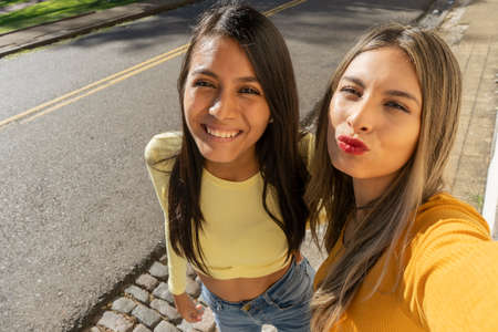 Dos hermosas mujeres jóvenes riéndose mientras se toman una selfie con su teléfono celular. Concepto de tecnología, comunicaciones, alegría y amistad.