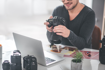 Smiling bearded man keeping professional camera while sitting at table in office labor concept copy space Stock Photo