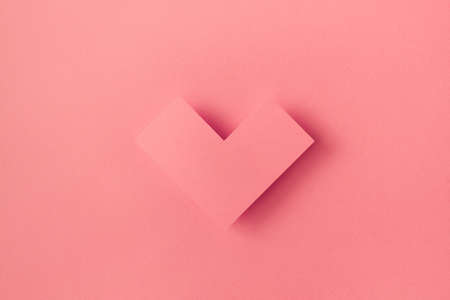 Geometric pink paper heart casting shadow on a paper background creative minimal love concept monochromatic flat lay idea