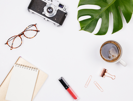 Travel blogger workspace with retro camera coffee cup notepad glasses lipstick and tropical palm leaf on white background flat lay for bloggers magazines social media and artists top view