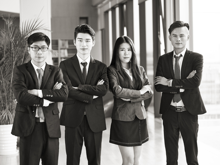 Portrait of a group of young asian business people standing in office arms crossed looking at camera black and white Stock Photo