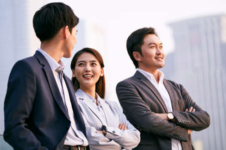 Team of three asian businesspeople talking chatting discussing business outdoors Stock Photo