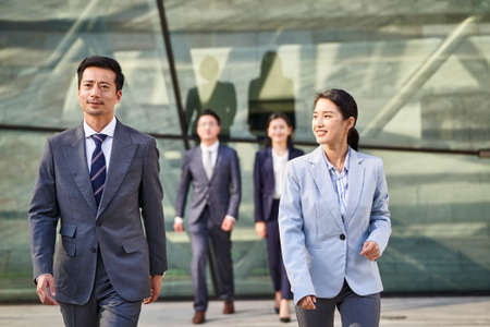 Group of four young asian business people walking outdoors on street in modern city