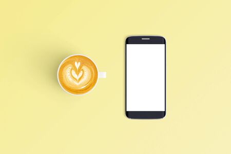 Top view of cup of coffee in a white cup and smart phone on office desk background