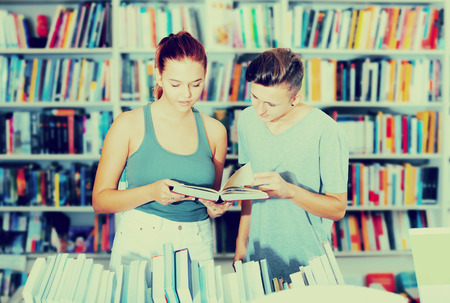 Portrait smiling teenager girl and boy holding open textbook in hands in book store