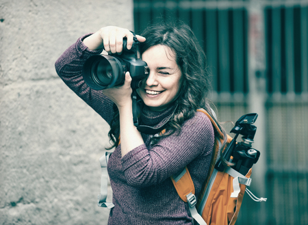 Cheerful woman taking picture with camera outdoors in town