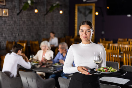 Young female waitress stands with order tray in spacious guest room in restaurant