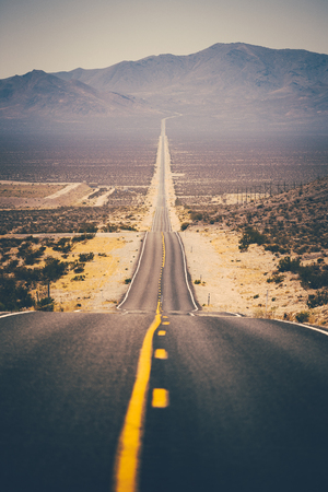 Classic panorama view of an endless straight road running through the barren scenery of the american southwest with extreme heat haze on a beautiful sunny day with blue sky in summer Stock Photo