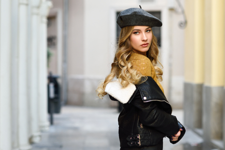 Blonde russian woman in urban background beautiful young girl wearing beret black leather jacket and mini skirt standing in the street pretty female with long wavy hair hairstyle and blue eyes Stock Photo
