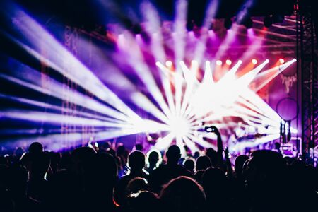 Concert crowd attending a concert people silhouettes are visible backlit by stage lights raised hands and smart phones are visible here and there