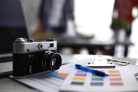 Laptop and camera on the desk two businesspeople standing in the background Stock Photo