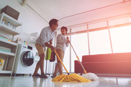 Happy Asian Father and Son está usando trapeadores para limpiar el piso de la casa juntos para el concepto de trabajo doméstico familiar. Foto de archivo