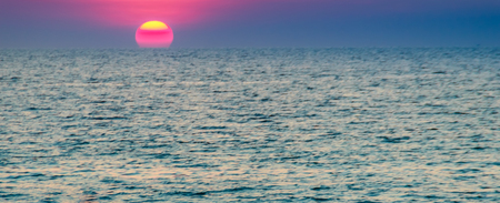 Hermosa puesta de sol sobre el mar, vista desde la playa. Sol redondo y brillante en la oscuridad sobre el mar en calma con fondo de cielo dramático borrosa.