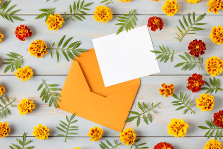 Sobre naranja con una hoja de papel en blanco para texto y flores de caléndula naranja sobre una mesa de madera azul concepto de escritorio de oficina festivo Foto de archivo