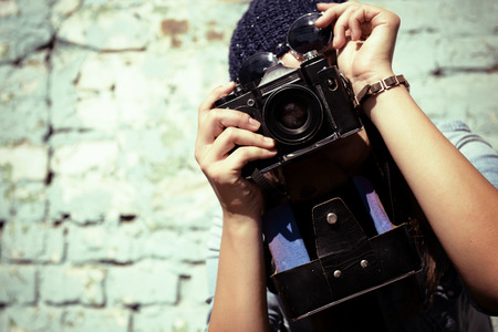 Retro photographer modern urban girl has fun with vintage photo camera outdoor near grunge wall image toned Stock Photo